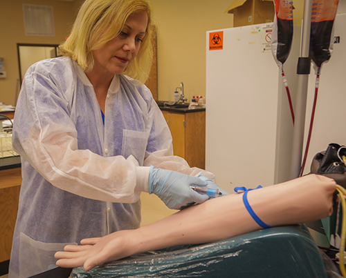 student drawing blood from a dummy arm