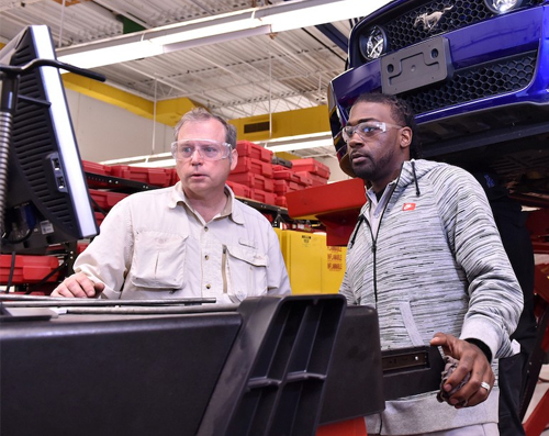 student looking at a computer with a car on a rack behind him