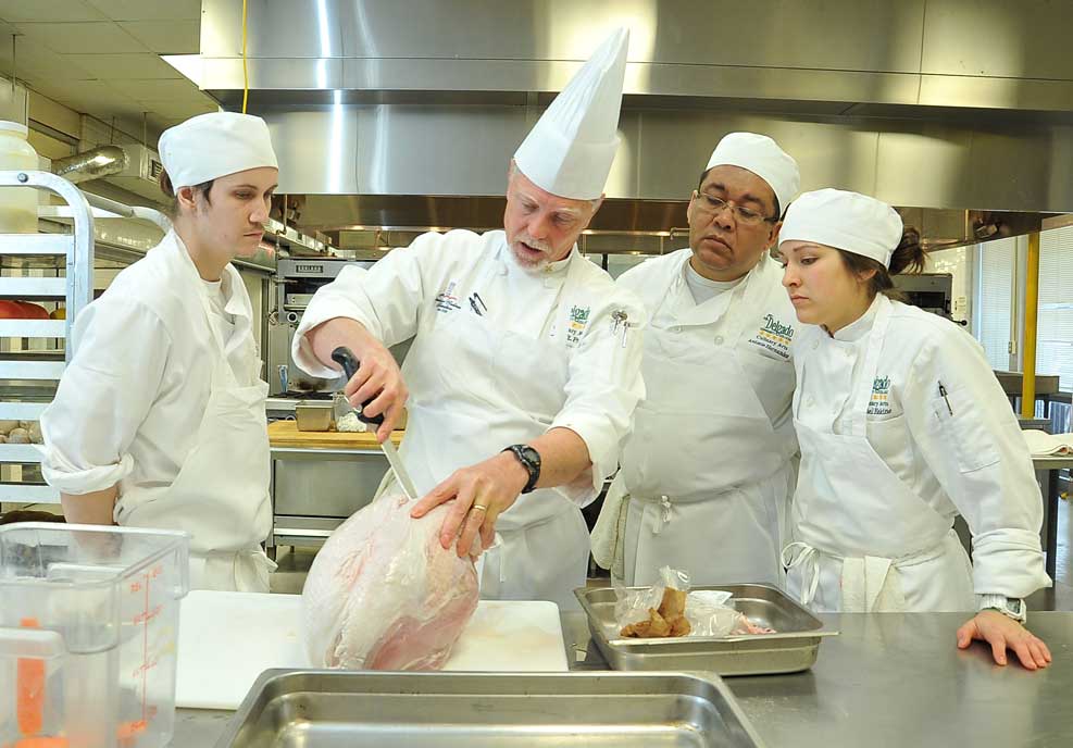 Delgado Culinary Arts student watches as their professor cuts into a raw chicken.