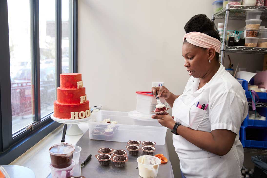A pastry chef spreads icing on a cupcake.