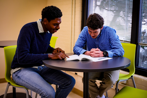 black male and white male sitting at a table looking at a book