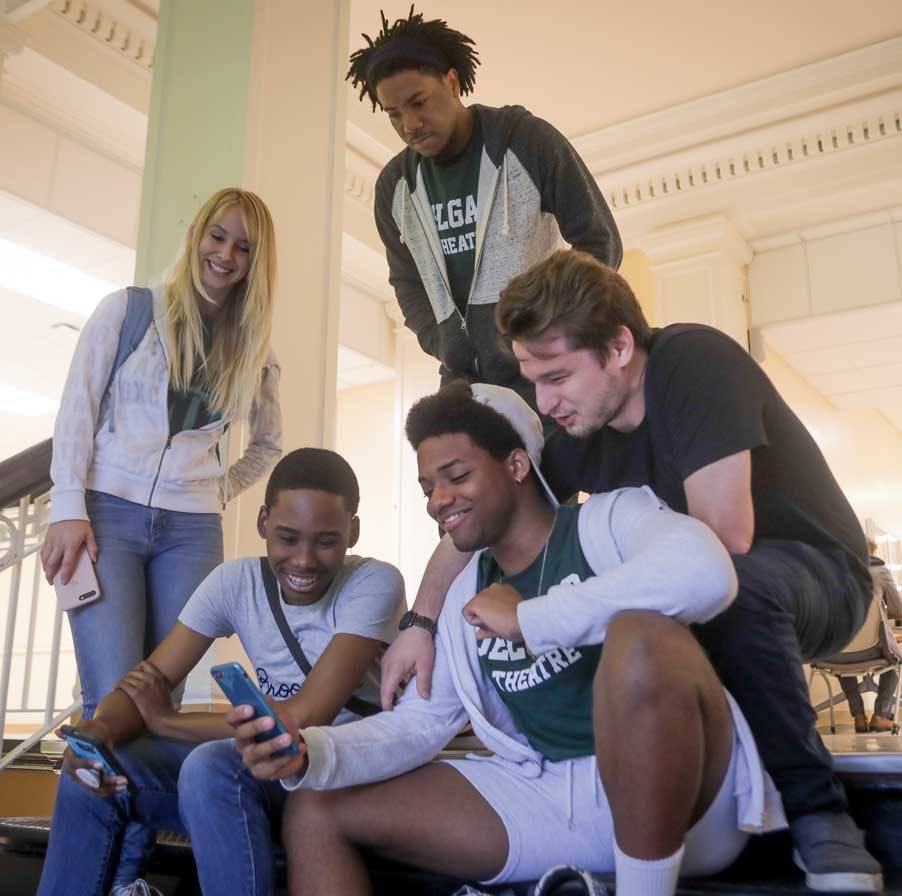 A group of five Delgado students laugh as one student shows off the contents of his cell phone screen.