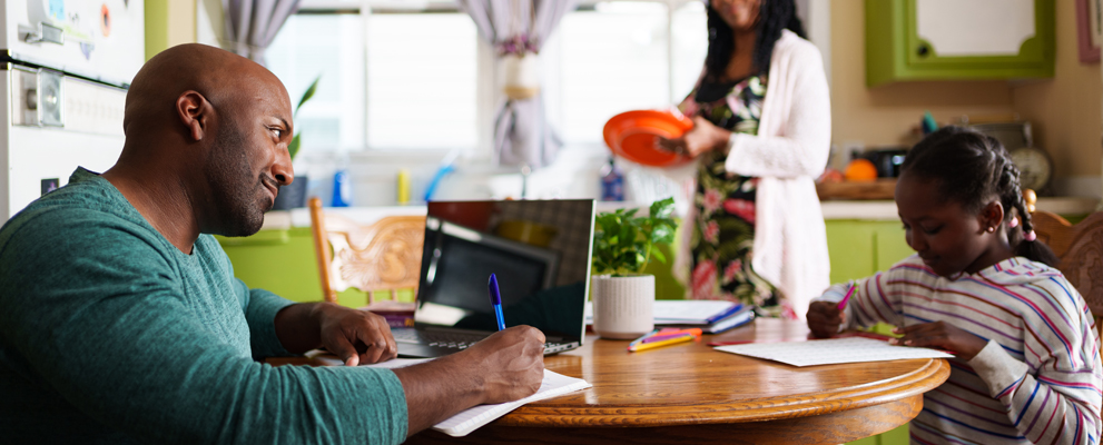 family in a kitchen with father and daughter doing school work