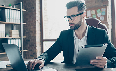 male working on a laptop with a tablet in his other hand